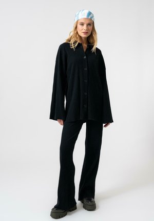 Camicia button-up nera a costine con maniche lunghe abbinata a pantaloni svasati coordinati. Presenta una vestibilità comoda e un tessuto testurizzato. Le calzature sono chunky nere.