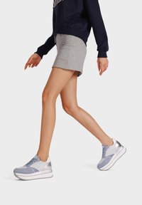 Sneaker blu chiaro e grigio con accenti argentati, pannelli testurizzati e suola imbottita. Indossato con una gonna grigia e un felpa scura.