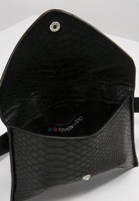 Borsa a mano nera in materiale sintetico con un motivo a croco testurizzato, chiusura a scatto magnetico e un interno in tessuto con etichetta del marchio.