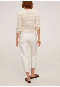 Sweter z dzianiny w kolorze kremowym z teksturowanymi wzorami, w połączeniu z białymi, krótkimi dżinsami o wysokim stanie z postrzępionymi brzegami i brązowymi klapkami.