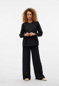 Czarny, długi rękaw, luźny top z wiązaniem, zestawiony z czarnymi spodniami o szerokich nogawkach. Gładka tkanina o minimalistycznym wzornictwie.