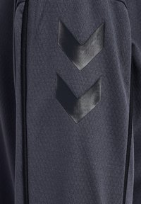 Ciemnoszara tkanina z dwoma czarnymi matowymi kształtami w formie szewronu ułożonymi pionowo, ukazującymi strukturę i subtelne fałdy materiału.