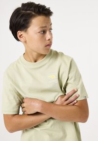 Camiseta de algodón verde claro con cuello redondo, mangas cortas y un logotipo gráfico en el pecho. Presenta una etiqueta en la manga izquierda.