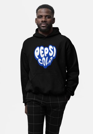 Mand iført sort hoodie med et stiliseret blåt og hvidt "Pepsi Cola" logo, parret med sorte bukser med et hvidt rutenet-mønster.