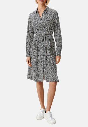 Schwarz-weiß gemustertes Hemdkleid mit langen Ärmeln, gebundenem Taillenzug und Knopfverschluss, kombiniert mit weißen Turnschuhen. Weicher Stoff.