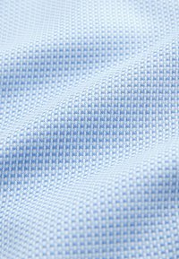 Svetlomodrá tkanina so vzorom zrnovej siete. Materiál je mäkký a pružný, s hladkým povrchom a rôznou hrúbkou nite.