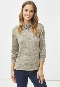 Top de cuello alto color gris claro hecho de tela de punto texturizada, con mangas largas y un pequeño bolsillo en el pecho, combinado con jeans de mezclilla oscura.