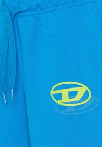 Pantaloni della tuta blu con cintura elastica e coulisse, caratterizzati da un logo giallo e una texture liscia. Progettati per il comfort e l'uso casual.