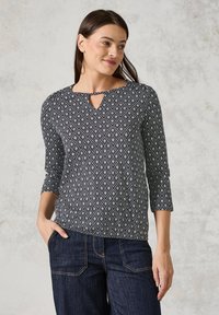 Svart- och vitmönstrad topp med en nyckelhålsringning, trekvartsärmar och en bekväm passform, som matchas med mörka jeans.