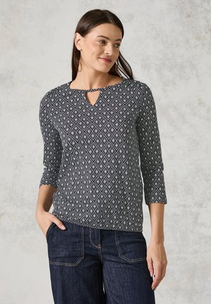 Svart- och vitmönstrad topp med en nyckelhålsringning, trekvartsärmar och en bekväm passform, som matchas med mörka jeans.