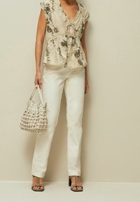 Beige tekstureret peplum-top med V-hals og bånd, parret med hvide lige jeans. Accessoriseret med en vævet bucket-bag og sandaler.