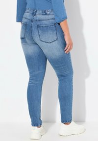 Vaqueros ajustados de mezclilla azul claro con una cintura de altura media, bolsillos traseros y una textura suave. Combinados con zapatillas blancas para un look casual.