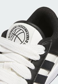 Černobílé basketbalové boty s texturovaným svrškem, výrazným logem na jazyku a plochými bílými tkaničkami se třemi černými pruhy.