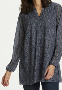 Navy blauwe blouse met lange mouwen van lichtgewicht, doorzichtig materiaal met een bloemenpatroon, voorzien van een subtiele V-hals en zijsplitsen voor gemakkelijk bewegen.