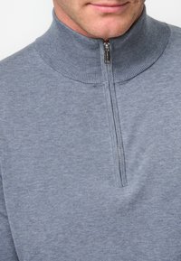 Grauer Zip-Hals-Pullover aus weichem Stoff, mit einem gerippten Kragen, einem durchgehenden Reißverschluss vorne und einer glatten Textur.