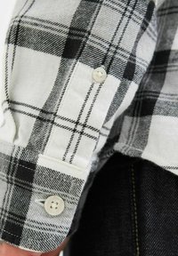 Zwart-witte geblokte flanellen shirt met een knoopmanchet en een zachte textuur, met opvallende horizontale en verticale lijnen in het patroon.