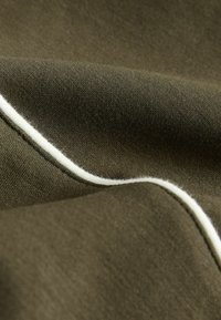 Tissu vert olive foncé avec une texture douce, présentant un accent de piping blanc le long du bord. Mettez l'accent sur la surface lisse du tissu et le contraste des couleurs.