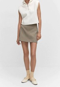 Haut blanc sans manches côtelé avec un col zippé, associé à une mini jupe à carreaux beige, des chaussures crème et des chaussettes texturées beiges.