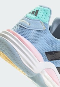 Zapatilla deportiva azul con parte superior de malla texturizada, acentuada por un collar verde menta, suela rosa y logo negro. Presenta una entresuela estriada y una suela exterior con patrón.