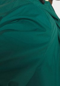 Chaqueta verde ligera con una textura suave, que presenta un cuello alto y toggles ajustables para un ajuste seguro.