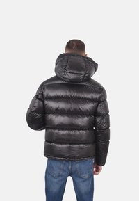 Giacca a vento nera con finitura lucida, cappuccio oversize e trapuntatura orizzontale. Indossata con jeans in denim blu, dal taglio casual.