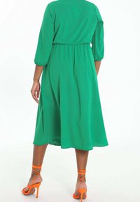 Grünes knielanges Kleid mit Dreiviertelärmeln, elastischem Bund und weichem Stoff, kombiniert mit orangefarbenen, schnüren High Heels.