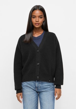 Schwarzer Strickcardigan mit V-Ausschnitt, der über eine Knopfverschlüsse, gerippte Bündchen und eine lockere Passform verfügt. Getragen über einem marineblauen T-Shirt und hellblauen Jeans.