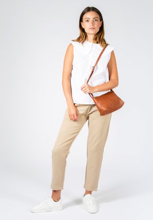 Blusa bianca senza maniche con scollatura arricciata, pantaloni beige a sigaretta e borsa a tracolla in pelle marrone. La modella indossa sneaker bianche.