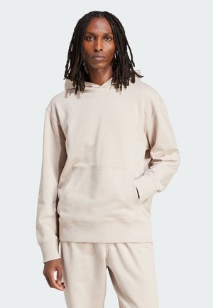 Sweat à capuche beige avec une poche frontale, coupe décontractée, poignets et ourlet côtelés, fabriqué en tissu doux, avec un petit logo sur la poitrine.