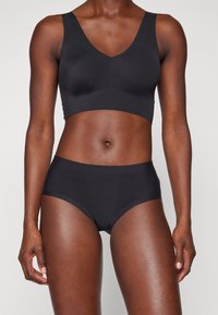 Black seamless bralette with a V-neck and wide straps paired with matching high-waisted briefs, smooth texture, and minimal design.