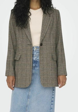 Woman wearing a beige ribbed top, checked blazer with single button, and high-waisted light blue denim skirt, hands relaxed by sides.