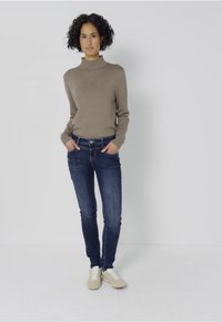 Beżowy sweter z golfem, niebieskie rurki i jasne trampki. Gładka tekstura, dopasowany krój i klasyczny styl.