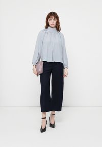 Ljusgrå blus med rynkade detaljer, hög krage och luftiga ärmar; ihop med marina vida byxor och svarta klackar med ankelrem.
