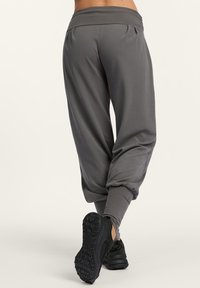 Person, der sich von einem hellen Hintergrund wegbewegt, trägt graue, weite Jogginghosen und schwarze Sportschuhe.