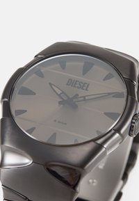 Schwarze Edelstahl-Armbanduhr mit rundem Zifferblatt, markanten Stundenmarkierungen und einem subtilen Farbverlauf-Layout mit dem "DIESEL"-Logo. Wasserdicht bis 5 Bar.