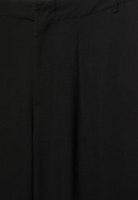 Czarne spodnie z gładkiego materiału z widocznymi zakładkami, płaskim przodem i boczną kieszenią. Talia ma standardową wysokość i małą szlufkę na pasek.