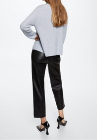 Maglione lavorato a maglia blu chiaro abbinato a pantaloni in finta pelle nera. L'outfit presenta una vestibilità comoda e tacchi a punta neri.