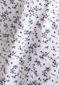 Tissu blanc avec un petit motif floral composé de fleurs bleues et d'accents rouges. Le design comprend des feuilles délicates et des tiges en noir.