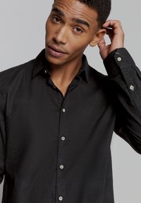 Zwart linnen overhemd met een button-down kraag, met een slim fit, lange mouwen en zilverkleurige knopen langs de voorkant en de manchetten.