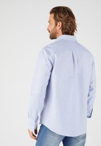 Camicia a righe blu chiaro e bianca con maniche lunghe e una piega sulla schiena. Progettata con colletto a punte e polsini con bottoni.