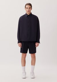 Donker marineblauwe oversized overhemd met kraag, gecombineerd met bijpassende shorts. Witte sneakers en crew-sokken maken de outfit compleet.