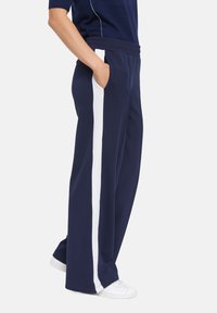 Marinblåa sweatpants med vit vertikal rand, elastisk midja, sidofickor och bred bendesign. Tillverkade av mjukt material.
