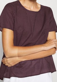 Bordeaux kortemouwtop met witte stippen, ronde halslijn, losse pasvorm en zachte stoftextuur. Geen zichtbare knopen of versieringen.