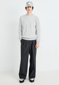 Un maglione grigio a coste abbinato a un pantalone a quadri grigio scuro e un cappello argentato. Le calzature presentano suole nere spesse con accenti metallici.
