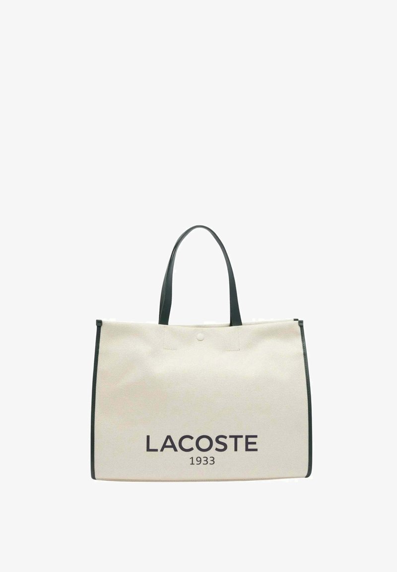 Sac en toile crème avec accents noirs, doté de doubles poignées et d'un grand imprimé à l'avant "LACOSTE 1933". Design simple et rectangulaire.