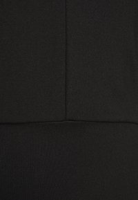 Gros plan sur un tissu noir avec une couture verticale en haut et une couture horizontale en bas, montrant les détails de la texture et des points.