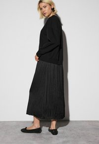 Black sweatshirt with a relaxed fit, paired with a pleated black maxi skirt. The outfit is complemented by black flat shoes with embellishments.