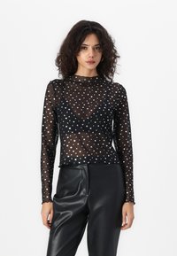 Svart mesh langermet topp med sølvstjernes mønster, høy hals og en tettsittende design. Kombinert med svarte skinnbukser.