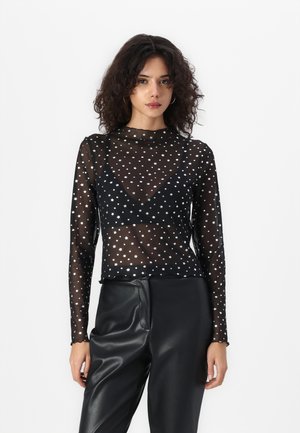 Svart mesh langermet topp med sølvstjernes mønster, høy hals og en tettsittende design. Kombinert med svarte skinnbukser.