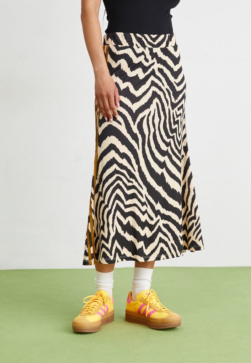 Zebra vzor sukni v černé a béžové barvě s elastickým pasem a rozšířeným designem, doplněná o jasně žluté tenisky a bílé ponožky.